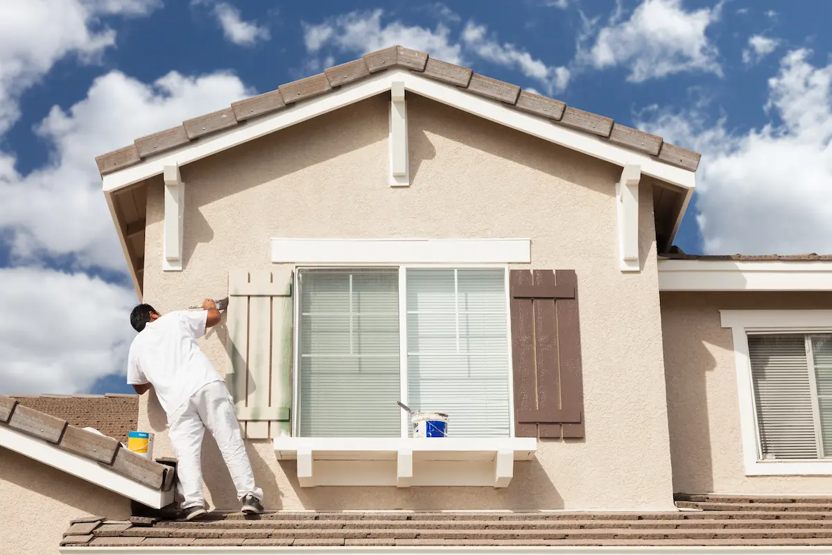 Professional house painter carefully painting exterior trim and shutters on a residential home