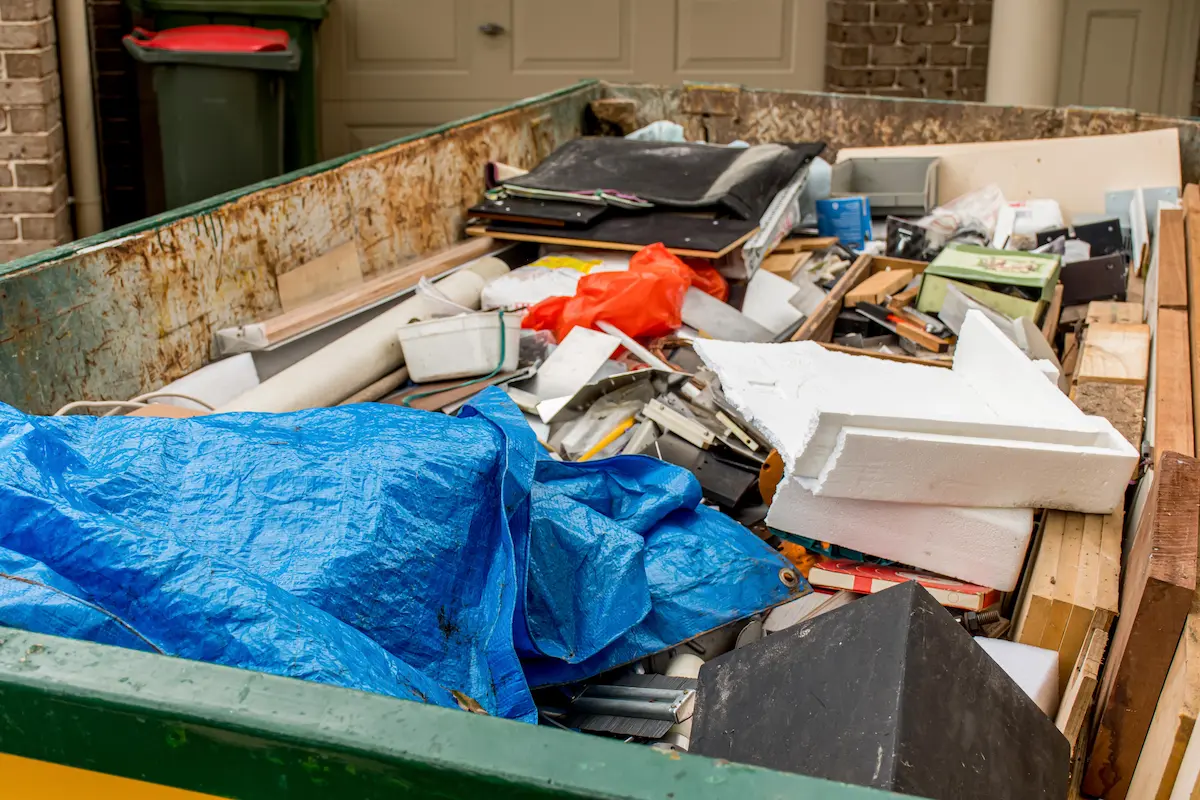 Large skip bin filled with household waste and rubbish in a front yard awaiting removal