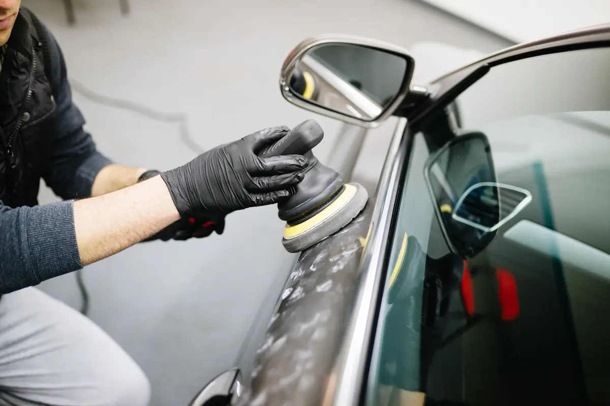 Auto detailing professional using an orbital polisher on a vehicle at a detailing shop