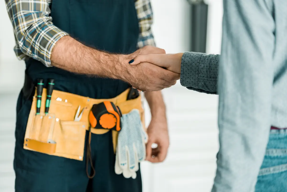 Handyman shaking hands with a homeowner customer in a kitchen after completing a repair job