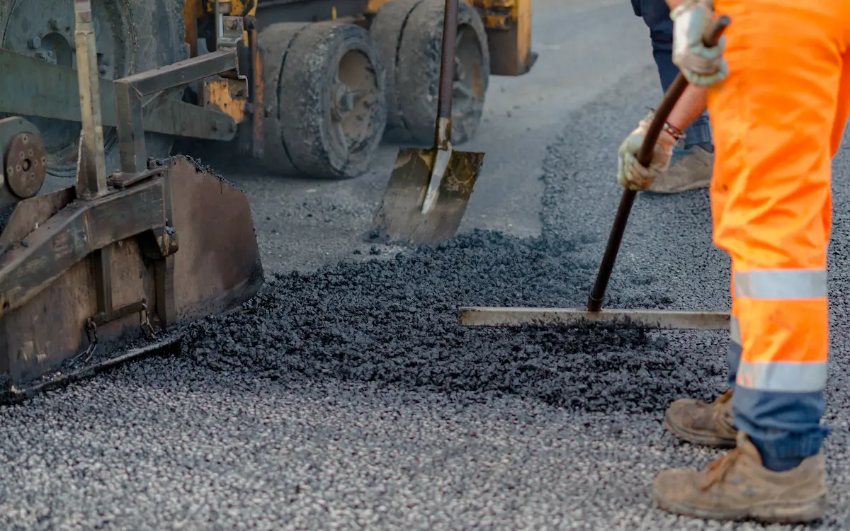 Asphalt paving crew operating a tracked paver machine laying fresh hot asphalt on a road