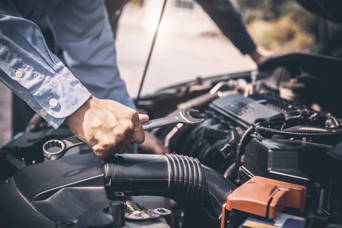 Auto mechanic hands using a wrench to repair a car engine during a mobile repair service call