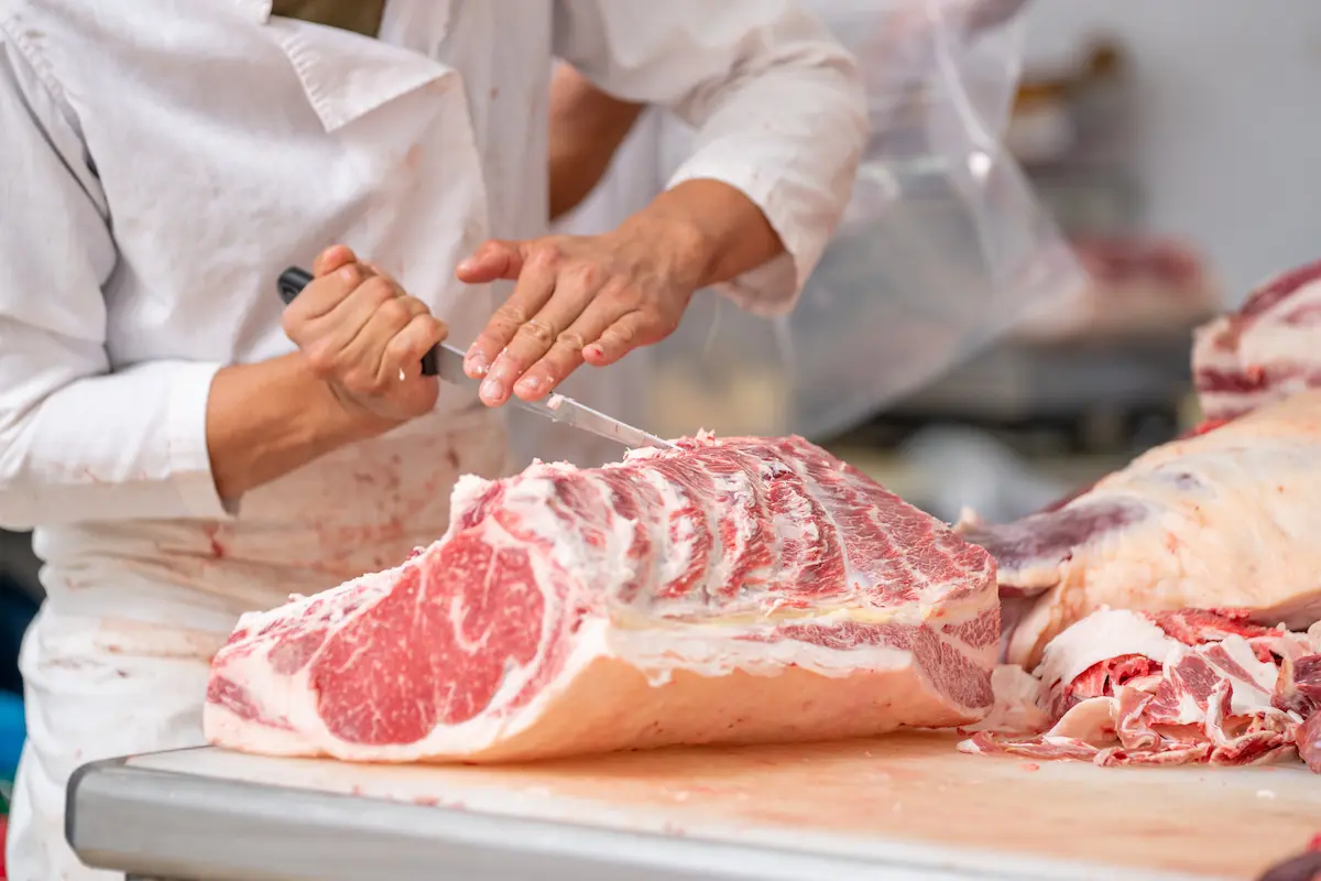 Professional butcher cutting raw wagyu beef with a knife on a butcher block table in a meat shop