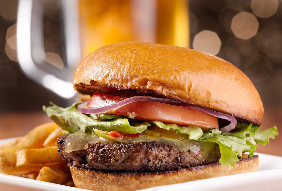Gourmet cheeseburger stacked high with fresh toppings with a cold mug of beer in the background
