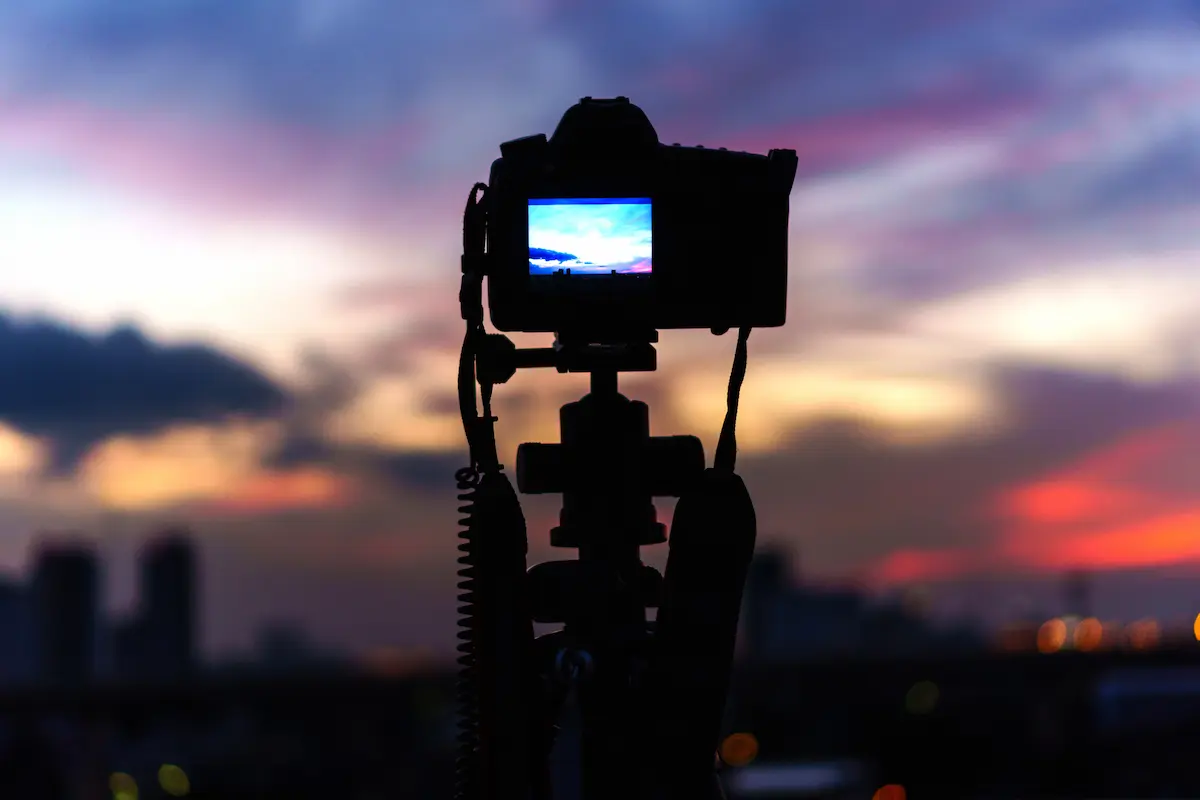 Silhouette of a camera on a tripod capturing a twilight landscape scene during a photography session