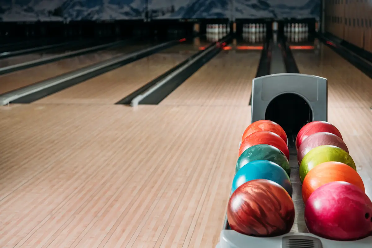 Colorful bowling balls on a rack in front of bowling alley lanes representing a vibrant family entertainment center