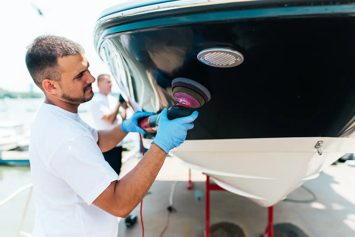 Professional boat detailer using an orbital polisher on a boat hull at a marina representing expert marine detailing services