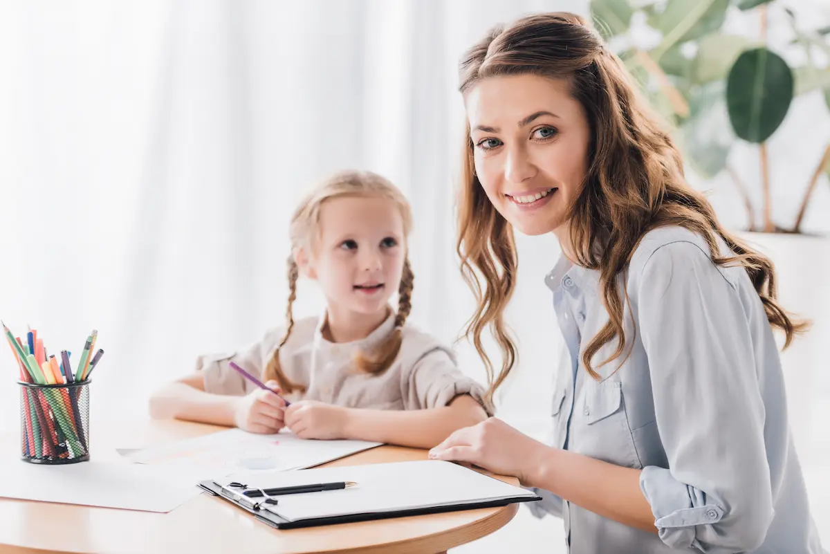 Smiling tutor working with a young child on drawing and learning activities representing the warm and encouraging environment of quality tutoring