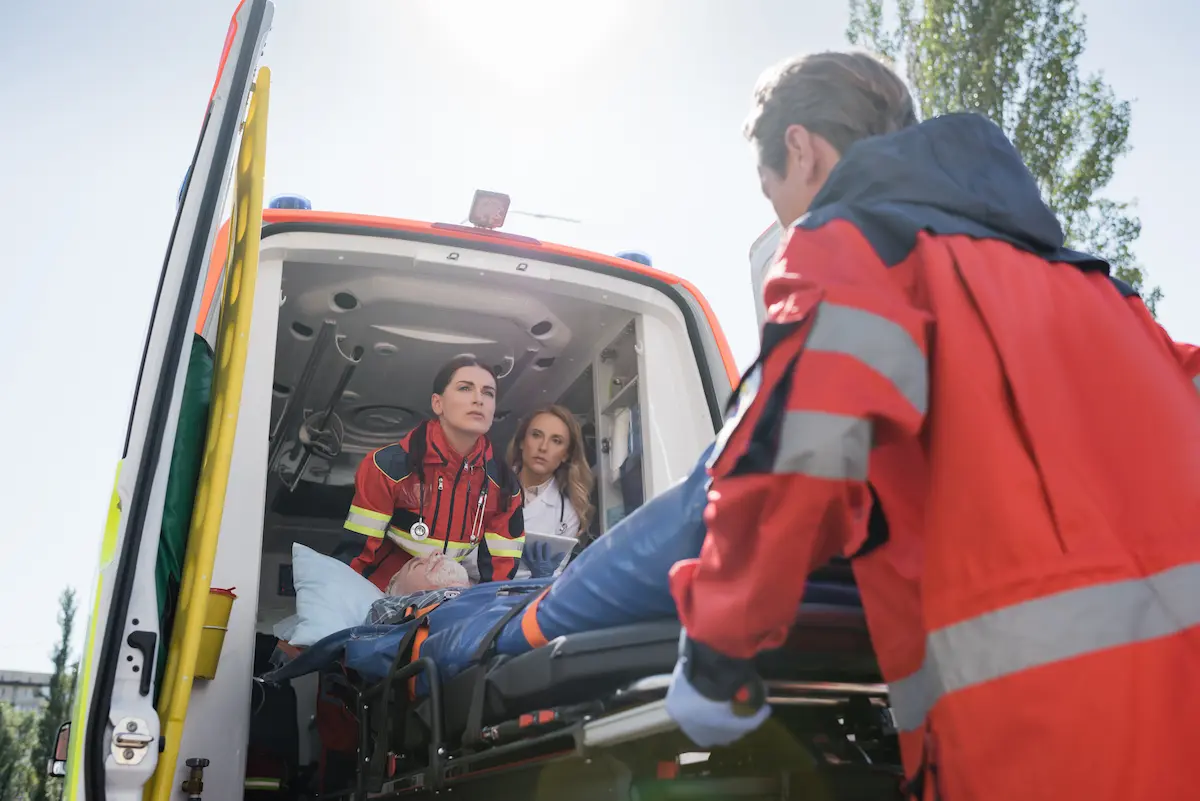 Paramedics carrying a patient on a stretcher to an ambulance representing the professional emergency medical response capability of a credentialed EMT service