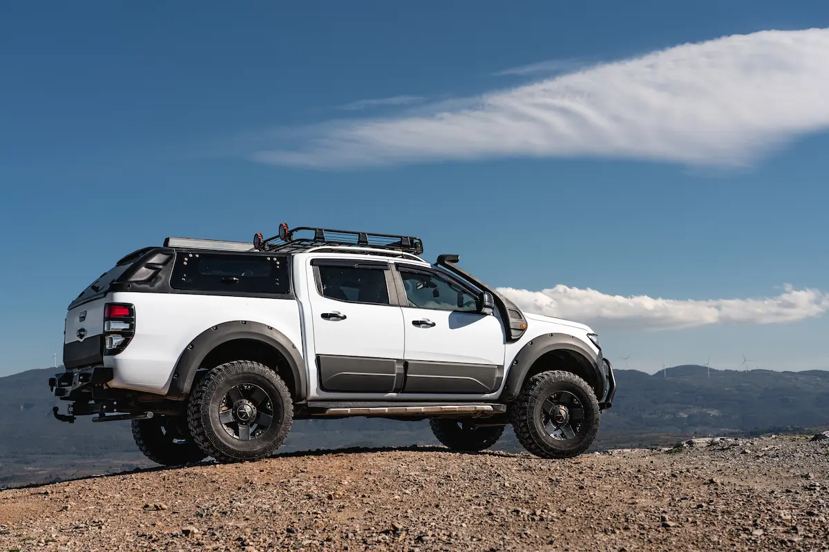 Custom-built 4x4 white Ford pickup truck on a deserted mountain road representing the quality builds and aftermarket accessories that truck enthusiasts pursue at a professional truck accessory store