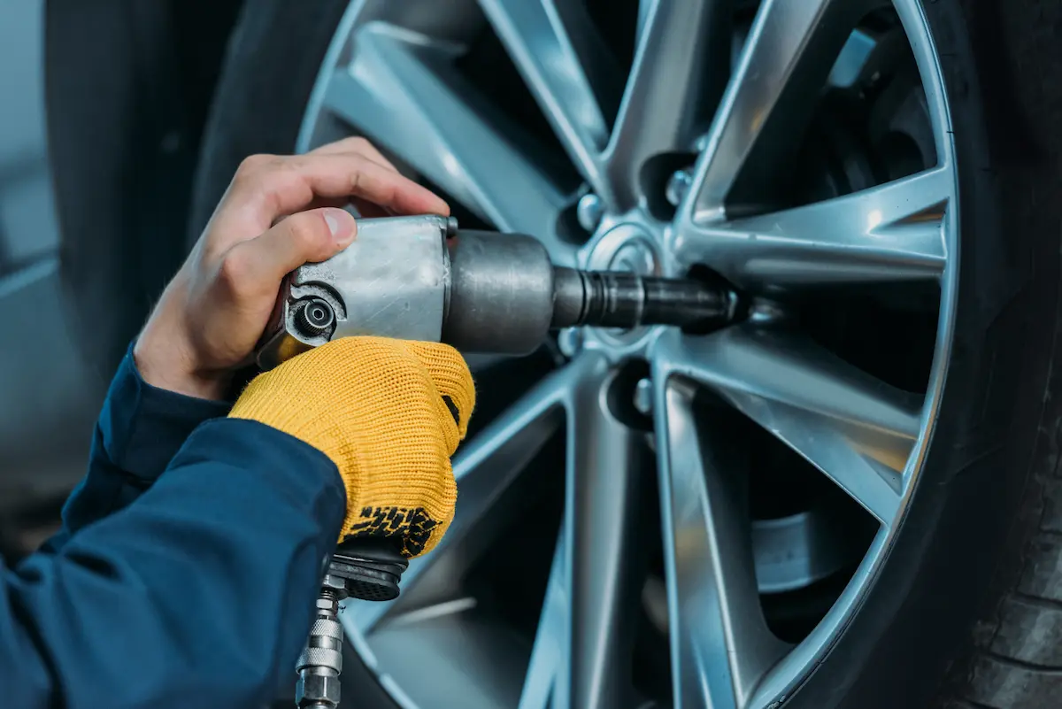 Auto mechanic unscrewing tire bolts representing the professional tire installation and wheel service offered at a quality tire and wheel shop