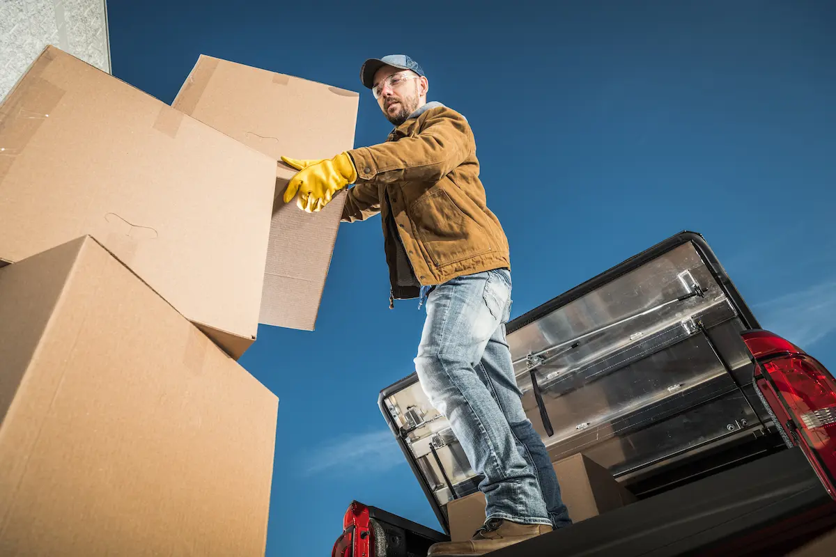 Moving company worker loading large cardboard boxes onto a cargo truck representing the professional and reliable residential and commercial moving services that a quality moving company provides