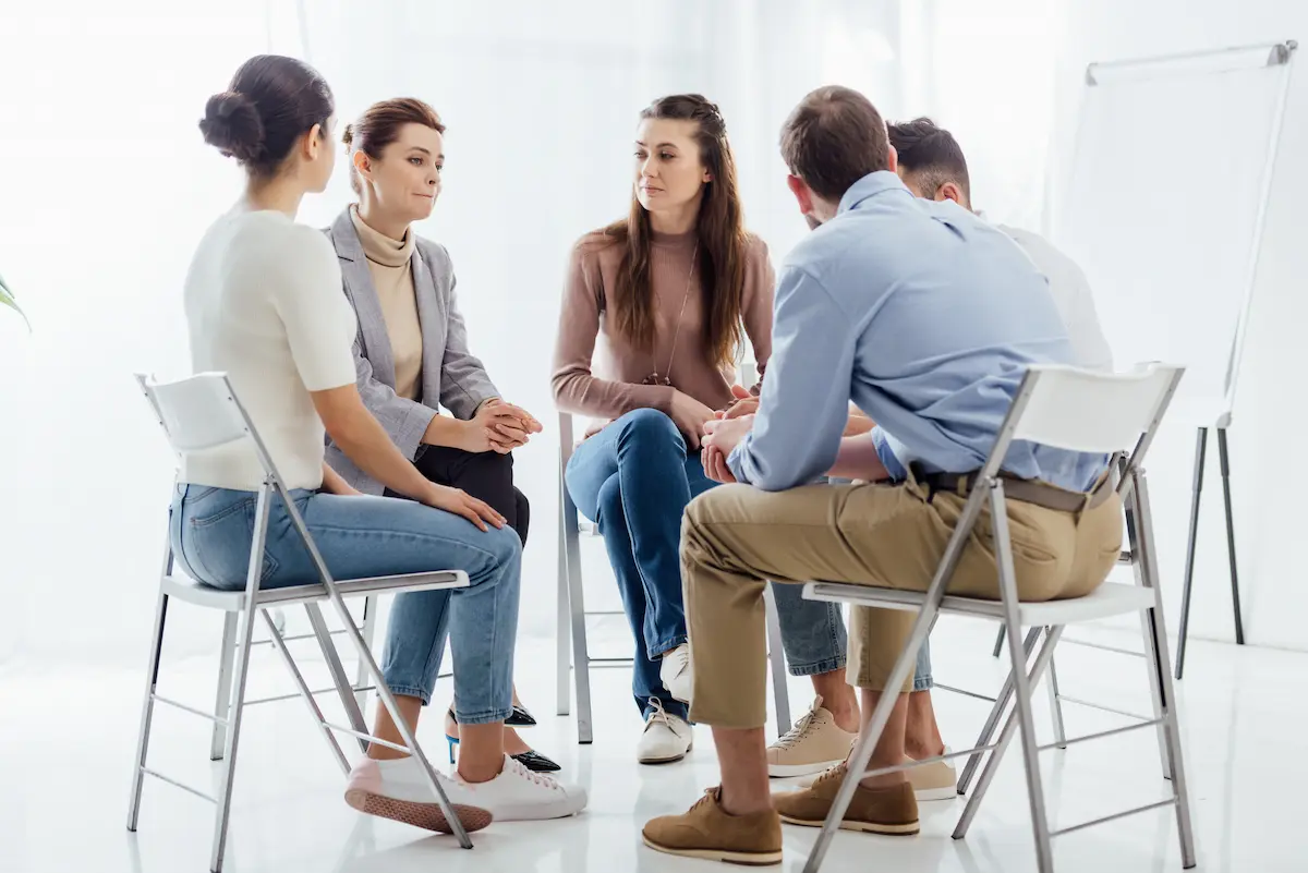 People sitting in a circle at a support group therapy meeting representing the peer community, accountability, and mutual support that a sober living home provides for individuals in early recovery