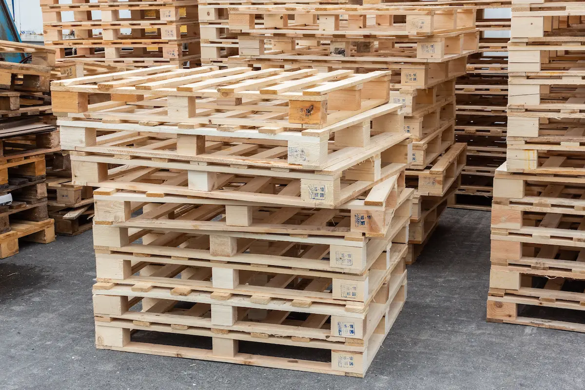 Wooden pallets stacked in a warehouse representing the commercial pallet supply inventory that a professional pallet supplier maintains for distribution, manufacturing, and logistics customers