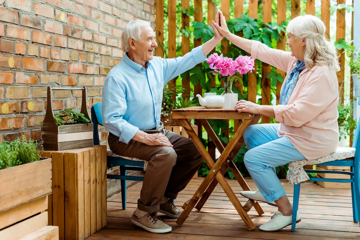 Cheerful senior couple sharing a high five while sitting among pink flowers representing the active, joyful, and socially connected lifestyle that a quality retirement community provides for its residents