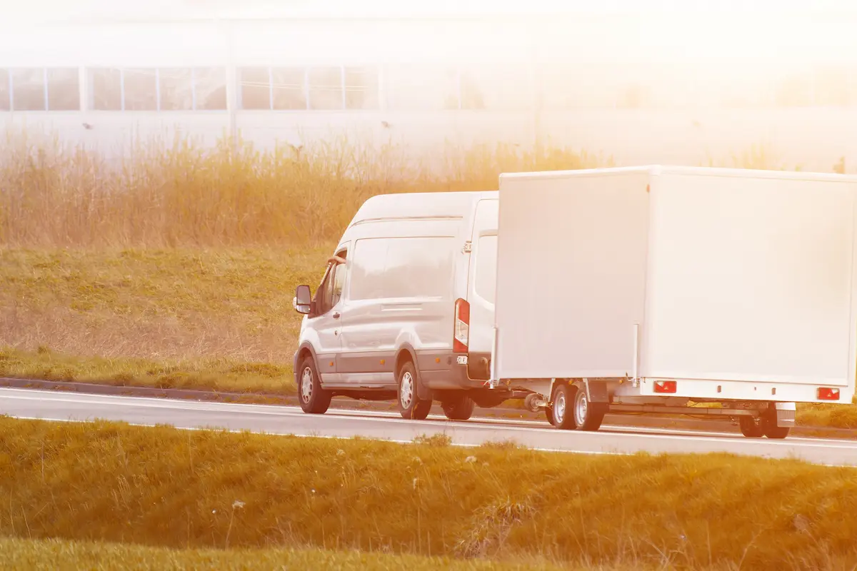 Vehicle towing a trailer on a bright rural highway representing the practical trailer hauling capability that a professional trailer rental company provides for homeowners and businesses