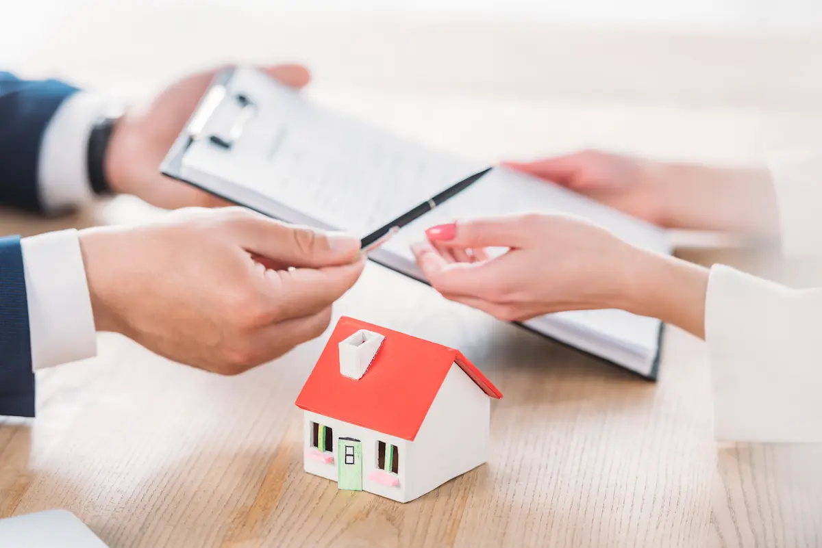 Mortgage professional giving a pen and loan agreement clipboard to a client representing the professional and guiding mortgage lending service that a qualified mortgage broker or loan officer provides for home buyers and homeowners