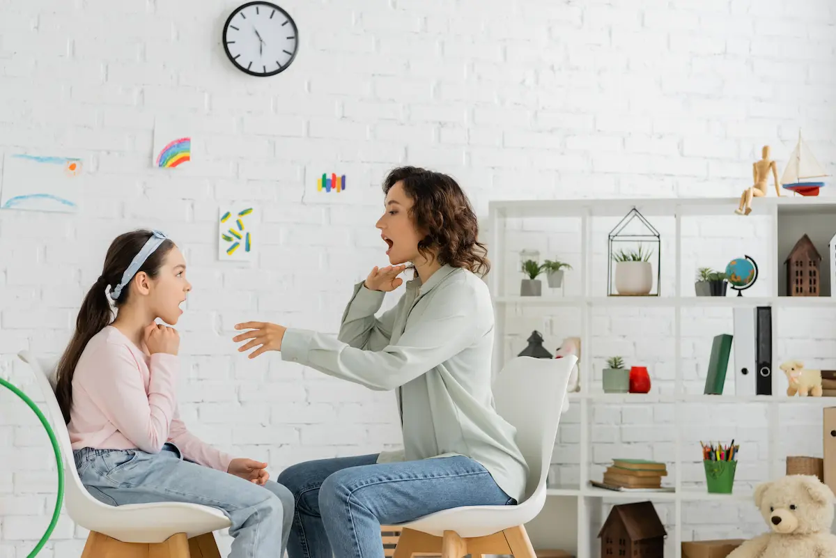 Speech therapist demonstrating mouth and articulation movements to a young patient in a consulting room representing the skilled and caring speech and language therapy that a qualified speech-language pathologist provides
