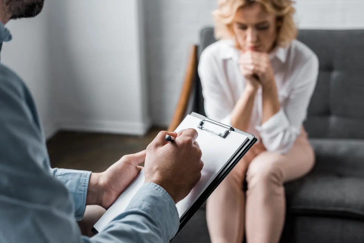 A woman in a therapy session with a clinician taking notes representing the compassionate and professional psychiatric care that a quality behavioral health clinic provides for patients seeking mental health and addiction treatment