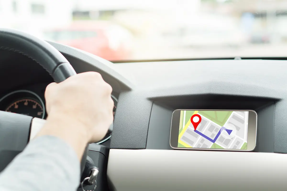 A man driving a car and navigating a rideshare app on his smartphone representing the active earning lifestyle that a reliable rideshare rental program enables for Uber and Lyft drivers