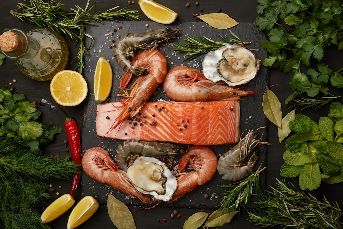 Fresh raw salmon and assorted seafood with herbs and lemons on a dark background representing the exceptional quality and freshness of ingredients that a great seafood restaurant sources and serves every night