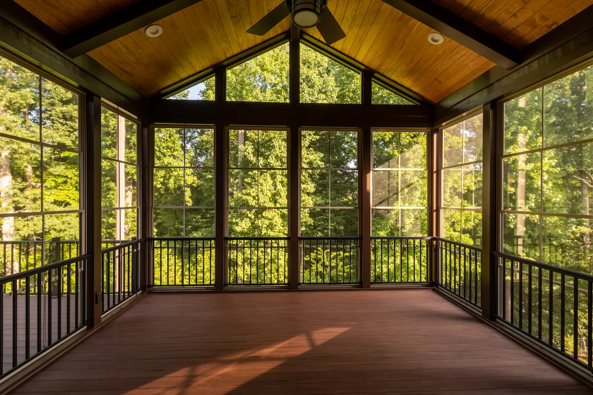 A modern screened porch with plastic windows and composite flooring surrounded by summer woods representing the quality outdoor living addition that a skilled screened enclosure contractor builds for homeowners