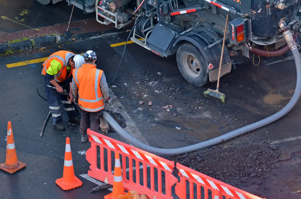 Road workers performing sewer and drain cleaning in a city street representing the professional and capable sewer maintenance service that keeps residential and commercial drainage systems flowing