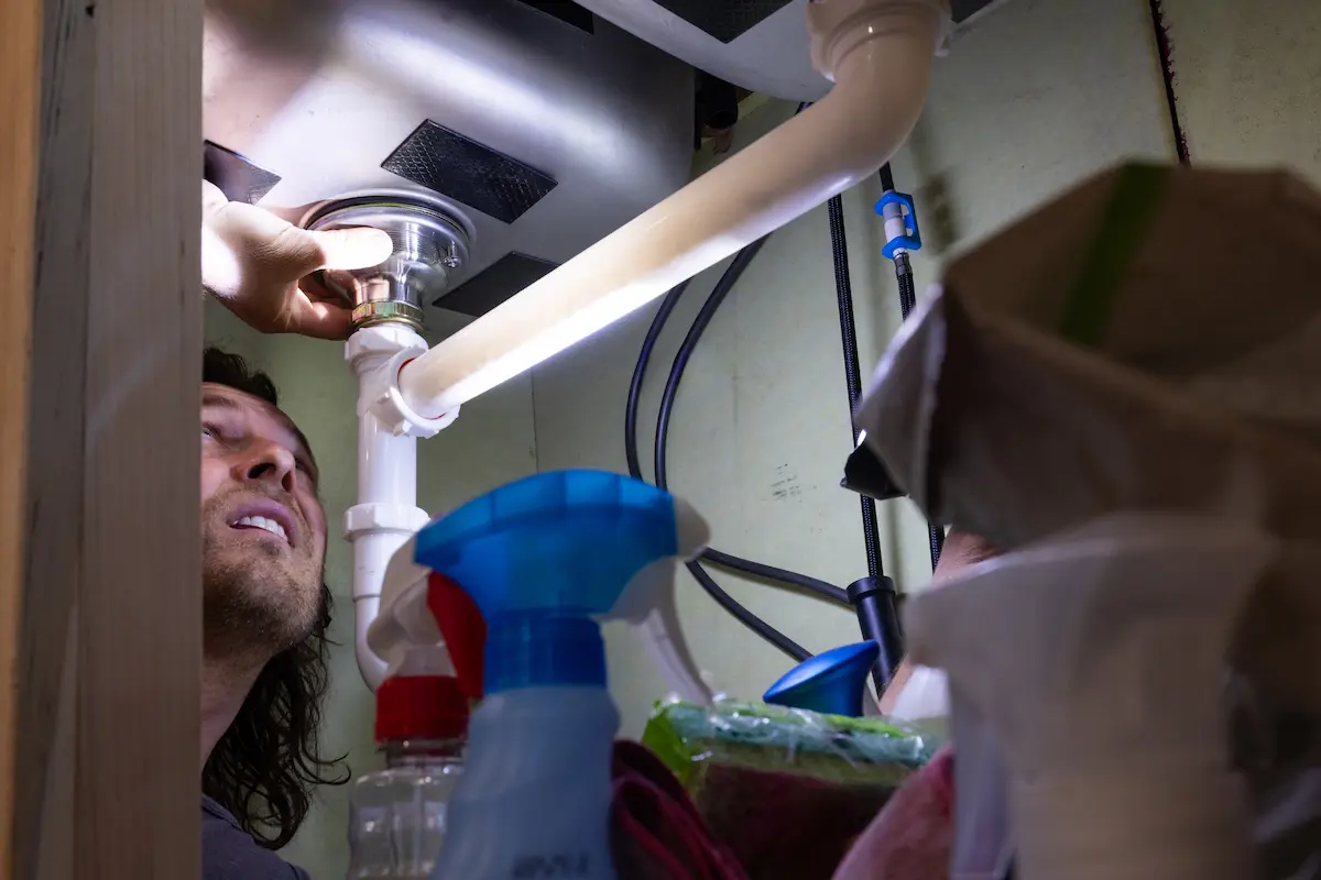 A professional using a flashlight to inspect and diagnose plumbing under a kitchen sink representing the careful investigative approach and technical expertise that a qualified leak detection company brings to every residential and commercial leak location service