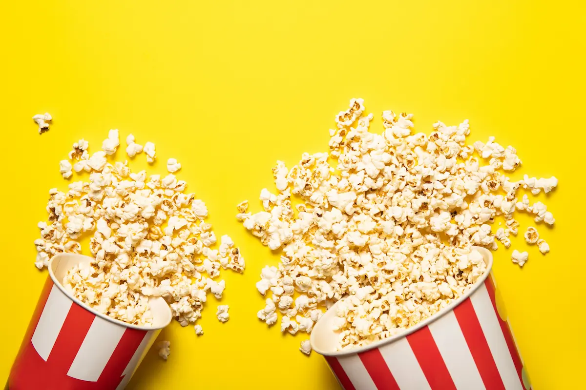 A paper cup of fresh popcorn on a bright yellow background representing the vibrant, appealing, and delicious popcorn products that make a well-run popcorn fundraiser the kind of program that supporters genuinely want to buy from and fundraising groups genuinely want to run