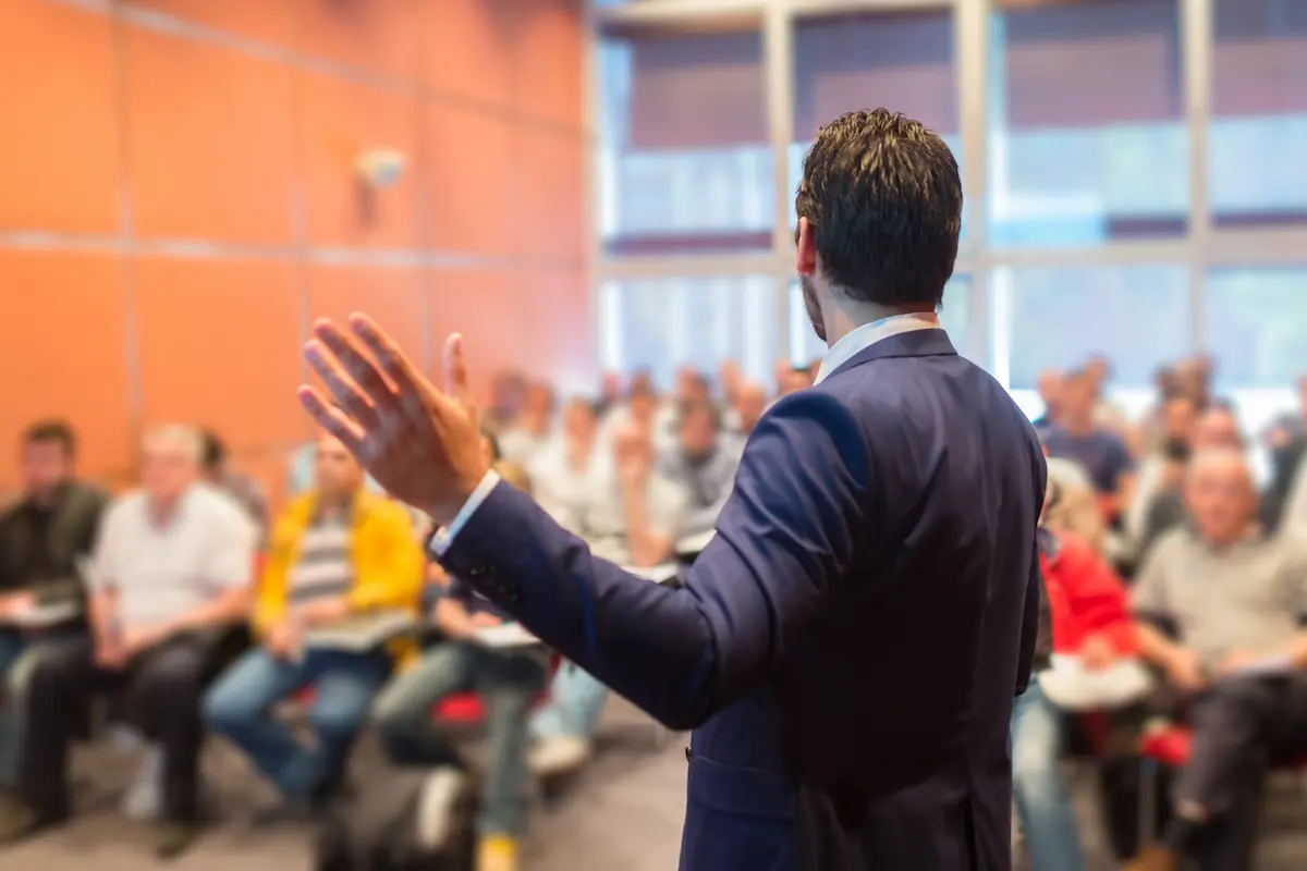 A professional speaker commanding a business conference stage representing the presence, clarity, and audience impact that a great keynote speaker delivers at every corporate event, association conference, and leadership summit