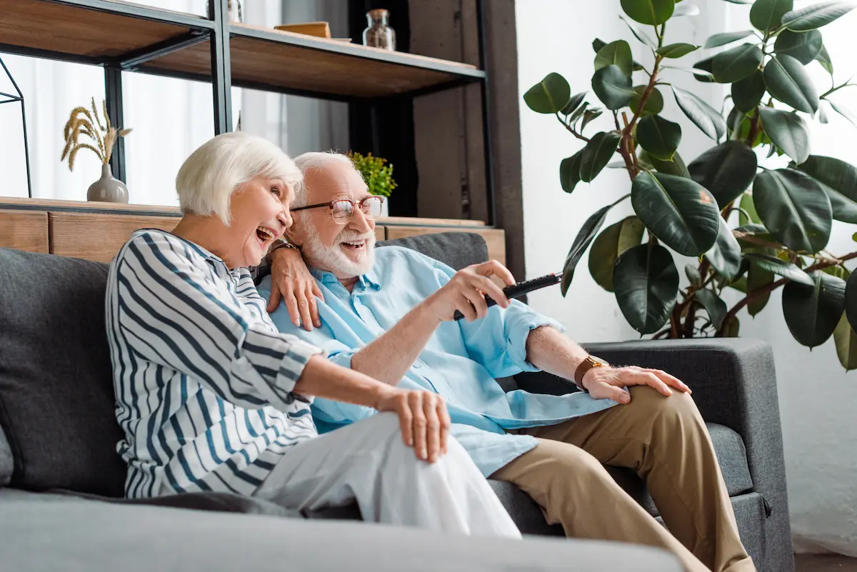 A cheerful senior couple relaxing together on a couch in their living room representing the comfort, dignity, and quality of life that a senior living advisor helps families find for their loved ones through compassionate guidance and local expertise in the senior care placement process