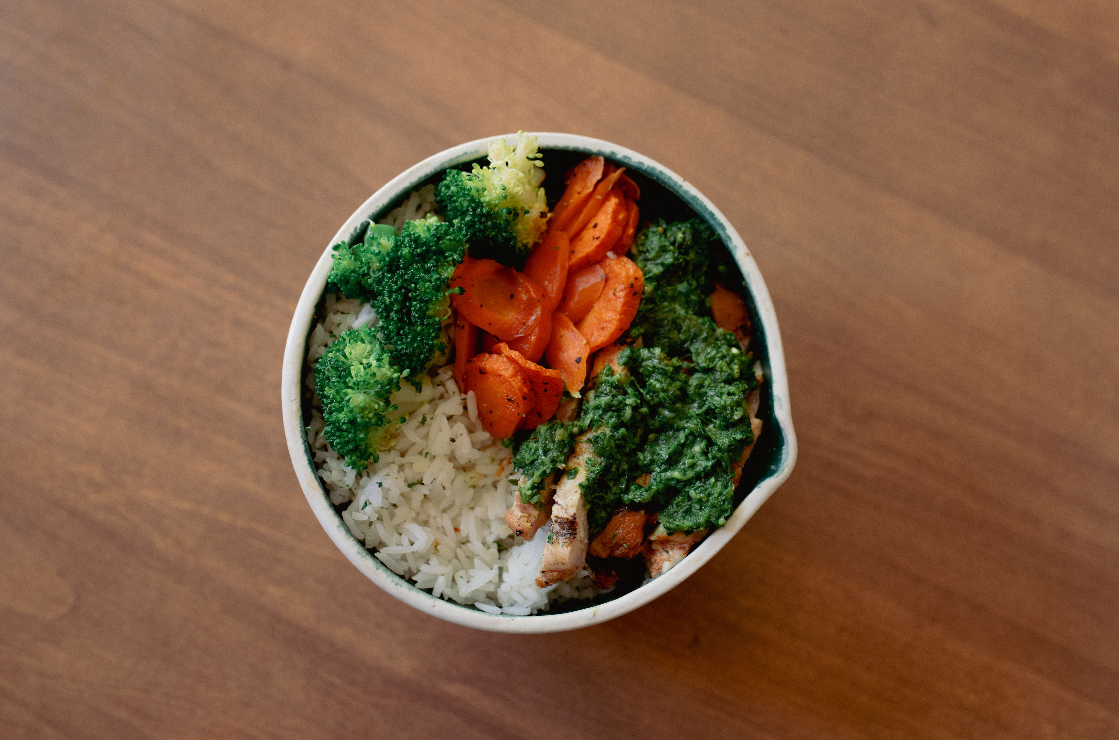 Pesto bowl with protein, jasmine rice, broccoli and carrots topped with green basil pesto